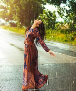 A woman gazes upward at the sky amidst a rainstorm, with traces of sunlight peeking through.